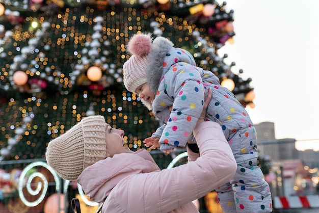 La giovane mamma felice vomita il bambino sullo sfondo dell'albero di Natale per strada