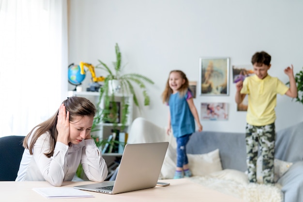 La giovane mamma lavora a casa con il portatile, insieme a due bambini. vogliono saltare