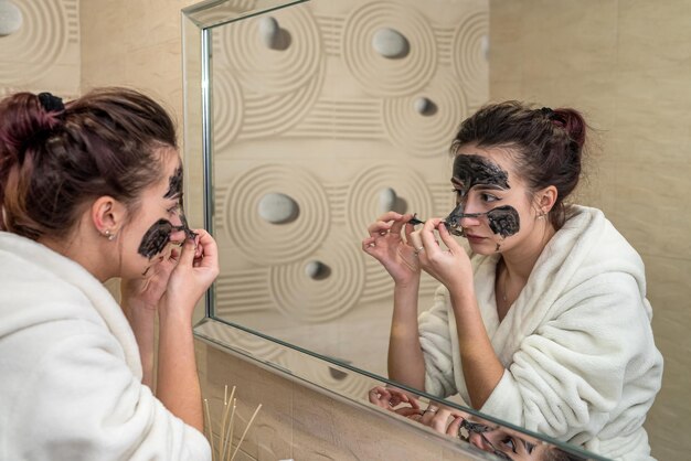 La giovane mora carina crea una splendida maschera nera di argilla da brufoli e punti neri Il concetto di cuscinetti per l'acne e i punti neri