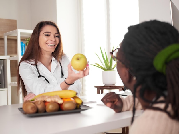 La giovane nutrizionista femminile in ufficio mostra una mela verde al suo paziente