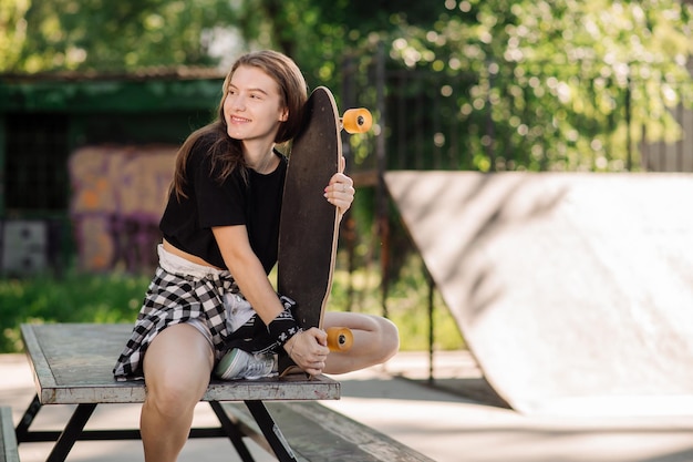 La giovane pattinatrice femminile è seduta con uno skateboard nel parco dei pattinatori