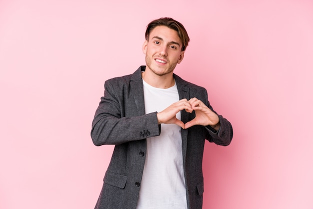 La giovane posa caucasica dell'uomo di affari ha isolato sorridere e mostrare una forma del cuore con le mani.