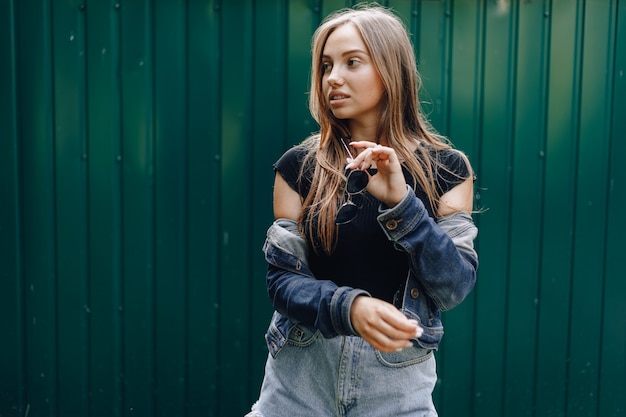 La giovane ragazza abbastanza attraente in vestiti del denim in vetri su una priorità bassa verde scuro semplice con il posto per testo.