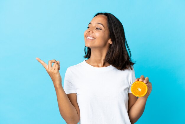 La giovane ragazza asiatica che tiene un'arancia sull'azzurro che intende realizzare la soluzione mentre solleva un dito