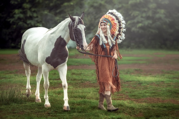 La giovane ragazza asiatica di bellezza con compone come la donna del nativo americano e cammina con il cavallo americano della pittura in Tailandia.