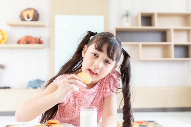 La giovane ragazza asiatica felice mangia il biscotto del biscotto del latte con il latte fresco del latte per colazione al mattino