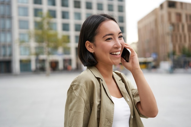 La giovane ragazza asiatica moderna parla sul telefono cellulare utilizza il telefono sulla strada della città donna sorridente durante la chiamata