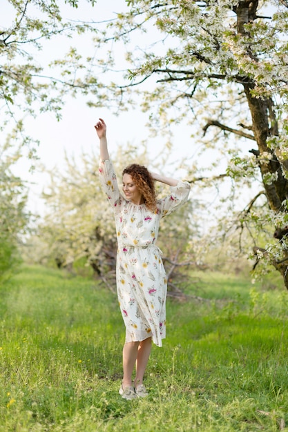 La giovane ragazza attraente cammina nel parco verde di primavera che gode della natura di fioritura