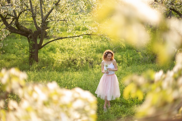 La giovane ragazza attraente cammina nel parco verde di primavera che gode della natura di fioritura