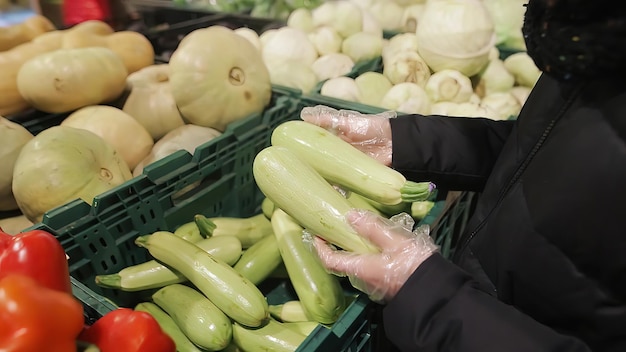 La giovane ragazza attraente sta raccogliendo le zucchine nel supermercato