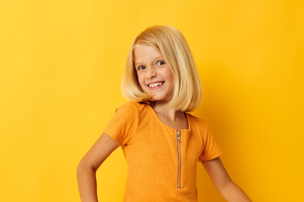 La giovane ragazza bionda in una maglietta gialla sorride in posa lo stile di vita dell'infanzia in studio inalterato
