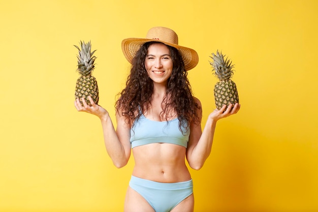 La giovane ragazza bruna riccia in costume da bagno blu in estate tiene in mano due ananas