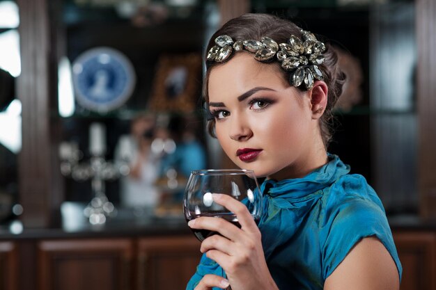 La giovane ragazza dai capelli castani sta bevendo e assaggiando un bicchiere di vino rosso secco