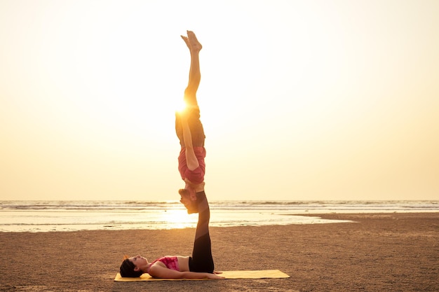 La giovane ragazza e il ragazzo delle coppie sportive stanno praticando esercizi di acroyoga al tramonto sulla spiaggia.