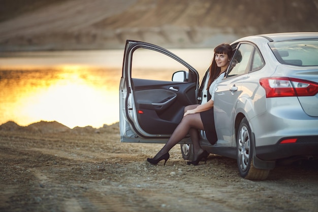 La giovane ragazza felice e bella del modello di grandi dimensioni si siede nella sua macchina sulla donna d'affari al tramonto che riposa dopo una dura giornata di lavoro