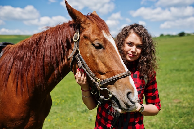 La giovane ragazza graziosa resta con il cavallo su un campo al giorno soleggiato.