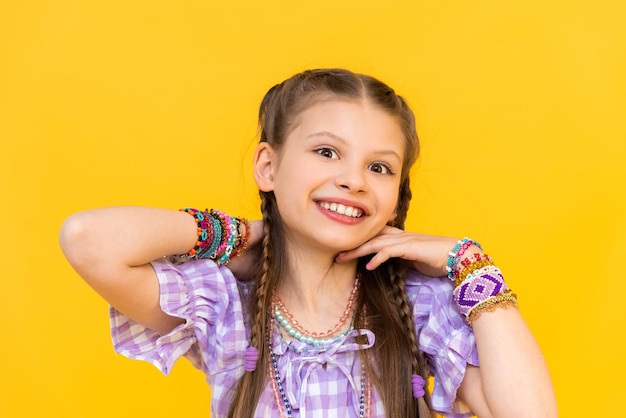 La giovane ragazza indossava un sacco di gioielli di perle per bambini e adolescenti Ritratto di una bambina braccialetti di perle sullo sfondo isolato giallo