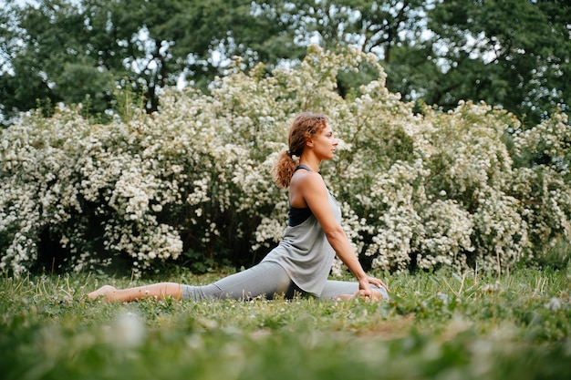 La giovane ragazza snella si dedica allo sport facendo esercizi di yoga equestre all'aperto nel parco esercizi di stretching orizzontale