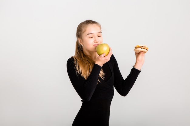 La giovane ragazza snella tiene un hamburger e una mela. scegliendo cibi sani, niente fast food