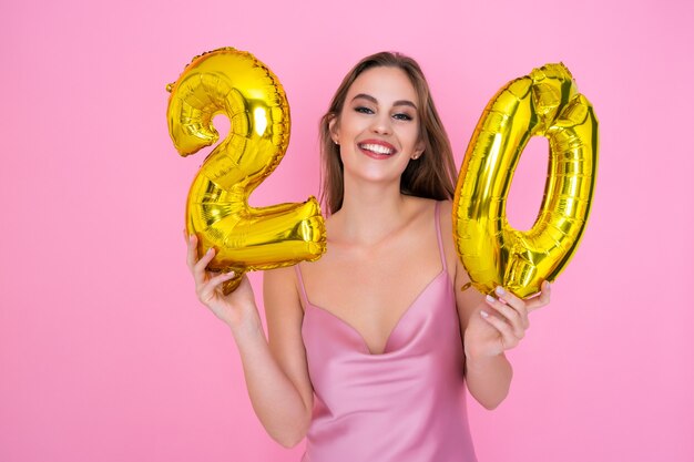 La giovane ragazza sorridente dell'adolescente tiene il pallone della lamina d'oro sul concetto rosa della festa di compleanno del fondo