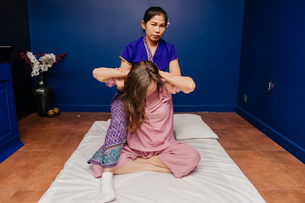 La giovane ragazza tailandese del lavoratore del massaggiatore in costume esotico asiatico etnico fa e dimostra le diverse procedure tradizionali della stazione termale nella stanza blu di yoga di rilassamento