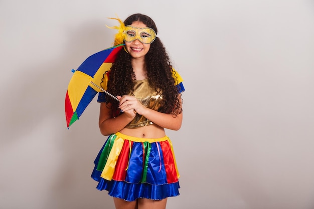 La giovane ragazza teenager brasiliana con il carnevale dei vestiti di frevo tiene l'ombrello di frevo che posa per la foto