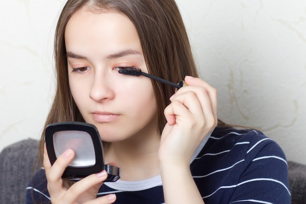 La giovane ragazza teenager fa un trucco naturale prima di andare a una festa o una passeggiata, dipinge le sopracciglia, le ciglia