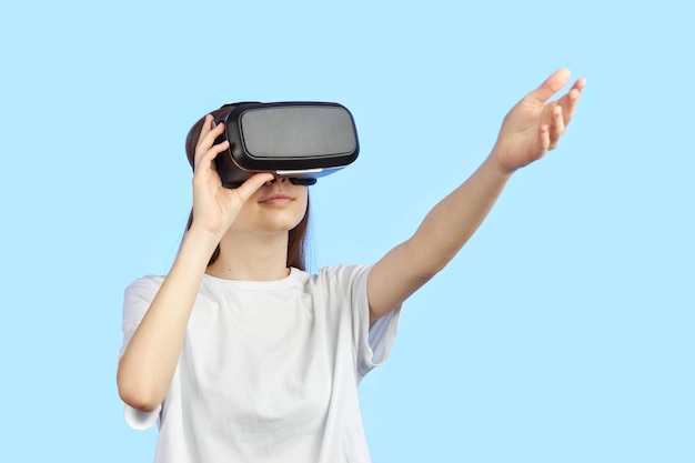 La giovane ragazza teenager in un casco di realtà virtuale isolato su una priorità bassa blu gioca un gioco per computer 3d