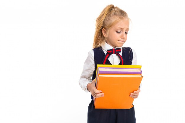 La giovane scolara con capelli biondi tiene molti libri isolati su fondo bianco