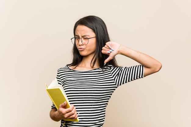 La giovane studentessa asiatica che tiene un libro si sente orgogliosa e sicura di sé, esempio da seguire.