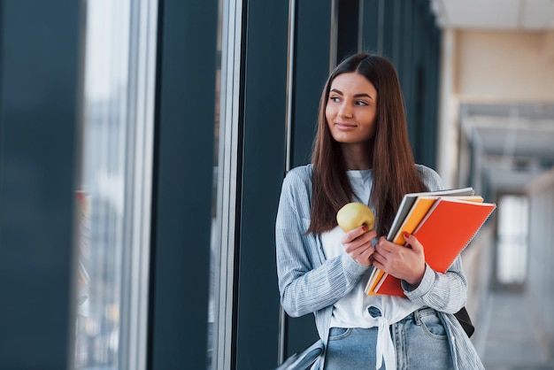 La giovane studentessa è nel corridoio di un'università che tiene i blocchetti per appunti e una mela