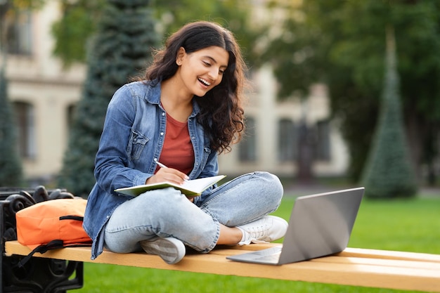 La giovane studentessa indù con il computer portatile e il blocco note studia all'aperto