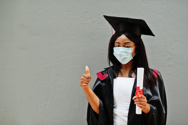 La giovane studentessa laureata afroamericana indossa una maschera protettiva contro il coronavirus. Concetto di cerimonia di laurea, quarantena.