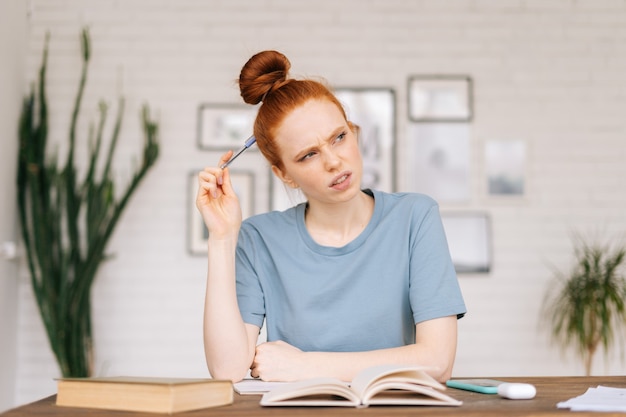 La giovane studentessa rossa premurosa sta facendo un contorno dal libro di testo nella cartella di lavoro