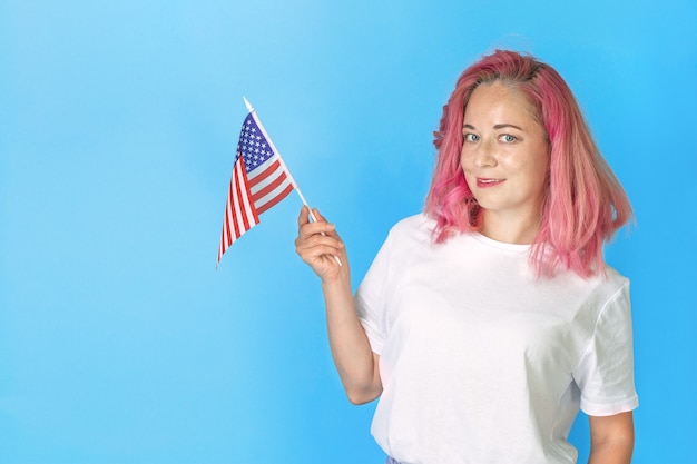 La giovane studentessa tiene la piccola bandiera americana e sorride su sfondo blu, donna felice che tiene la bandiera USA. Impara l'inglese. studio all'estero, corsi di lingua internazionale.