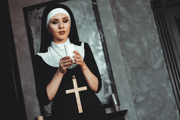 La giovane suora cattolica sta tenendo la candela nelle sue mani. Foto su sfondo nero. Vista laterale.