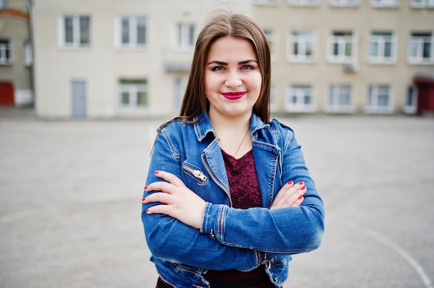 La giovane usura paffuta dell'adolescente sul rivestimento rosso dei jeans e del vestito ha proposto contro il cortile della scuola.