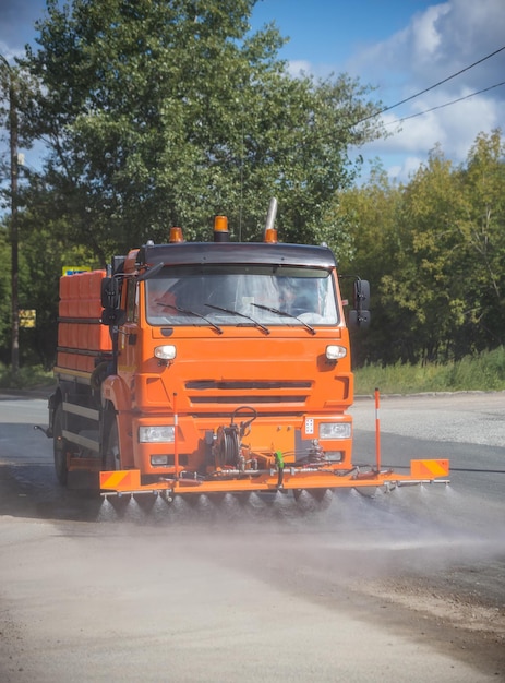 La grande macchina arancione pulisce l'asfalto con l'acqua