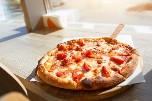 La grande pizza si trova su un tavolo in un caffè. Pizza italiana tagliata a pezzi.