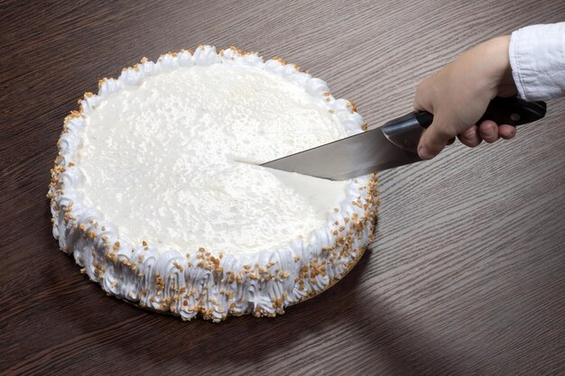 La grande torta bianca con una cima rumorosa viene tagliata con un coltello