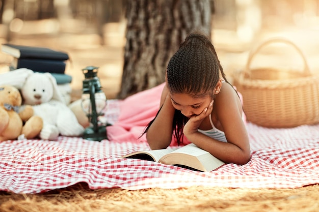 La lettura apre nuovi mondi per i bambini Inquadratura di una bambina che legge un libro con i suoi giocattoli nel bosco