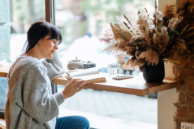 La lettura mi libera dalla noia. Giovane ragazza dell'allievo al libro di lettura del caffè.