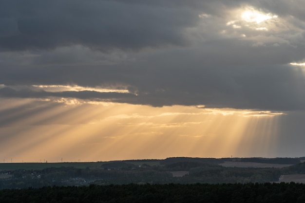 La luce del sole passa attraverso le nuvole in linea retta e cade sulla città e sulla foresta Il sole era nascosto dietro le nuvole La foresta nei raggi del sole al tramonto