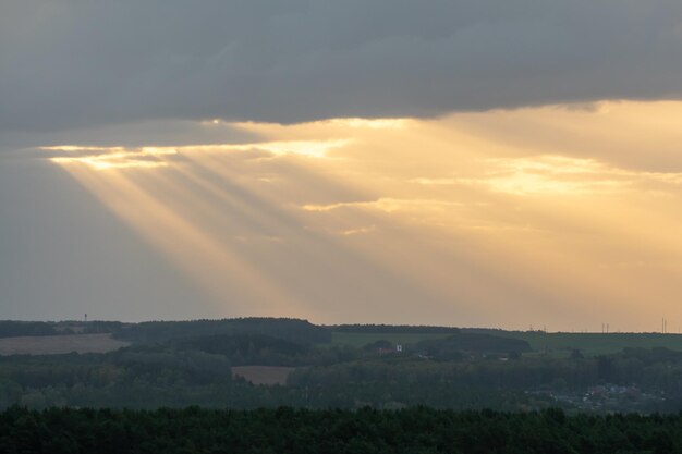 La luce del sole passa attraverso le nuvole in linea retta e cade sulla città e sulla foresta Il sole era nascosto dietro le nuvole La foresta nei raggi del sole al tramonto