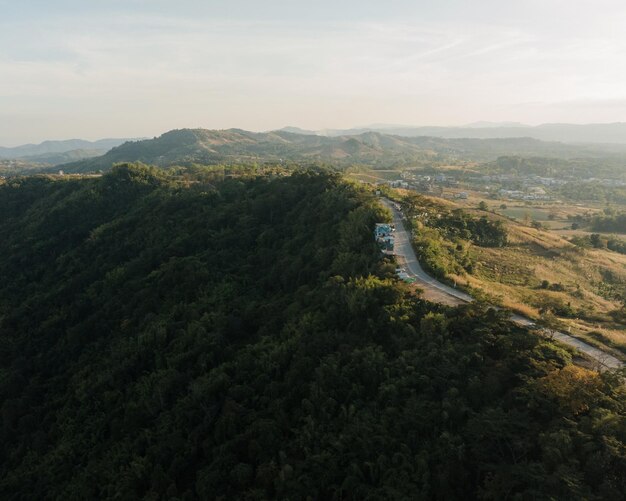 La luce del tramonto getta un leggero bagliore sulle colline boscose con una strada tortuosa che attraversa il paesaggio tranquillo