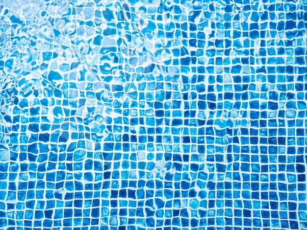 La luce riflessa sulla parte superiore della superficie dell'acqua della piscina rivestita con tessere di mosaico blu sotto Le increspature dell'acqua sullo sfondo della piscina con piastrelle blu