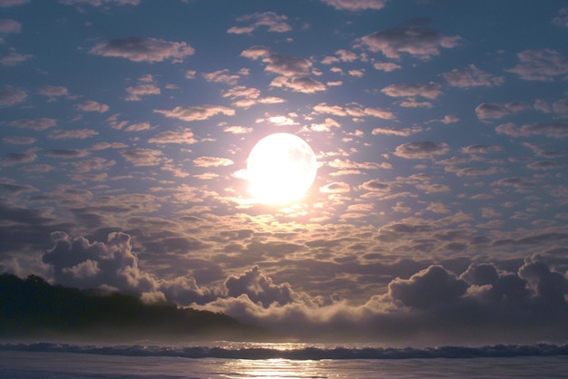 La luna e le nuvole creano un'atmosfera affascinante sopra l'oceano sereno.