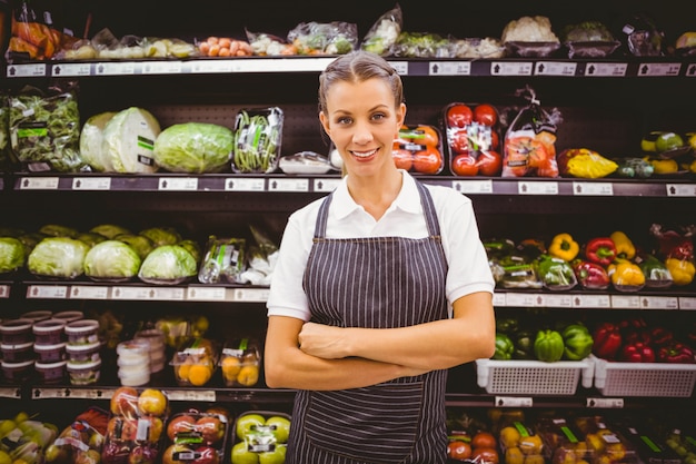 La macchina fotografica di sguardo bionda graziosa felice con le armi ha attraversato in supermercato