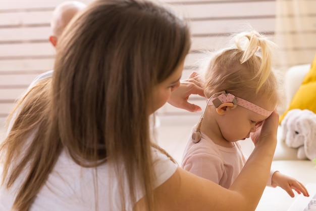 La madre aiuta il suo bambino a mettere su parte dell'impianto cocleare Bambino sordo con apparecchio acustico a casa diversità