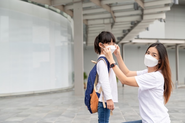 La madre asiatica aiuta sua figlia a indossare una maschera medica per la protezione Covid-19 o l'epidemia di coronavirus a prepararsi per andare a scuola quando torna a scuola.